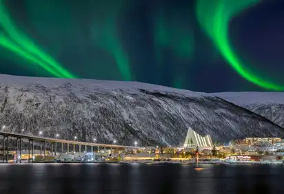 Polarlichter über schneebedeckten Bergen und Stadt bei Nacht.