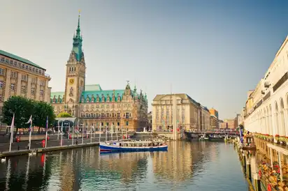 Hamburger Rathaus mit Wasserkanal und Boot im Vordergrund bei Sonnenschein.