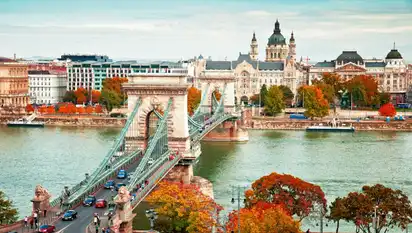 Historische Kettenbrücke über Fluss mit Stadt im Hintergrund.