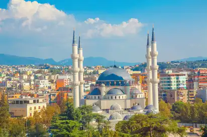 Große Moschee mit vier Minaretten vor Stadt- und Berghintergrund.