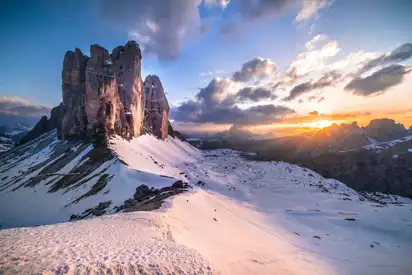 Verschneite Berglandschaft bei Sonnenuntergang mit Wolken am Himmel.