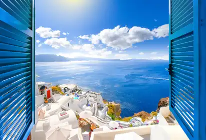 Blick aus einem Fenster auf Santorini mit weißem Dorf und blauem Meer.