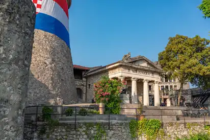Historisches Gebäude mit Säulen und Steinmauer im Vordergrund.