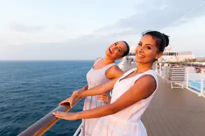 Zwei Frauen auf einem Kreuzfahrtschiff lachen beim Sonnenuntergang.