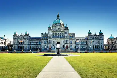 Historisches Gebäude mit Kuppeln und gepflegter Grünfläche davor.