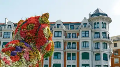 Große Blumenskulptur eines Hundes mit einem historischen Gebäude im Hintergrund.