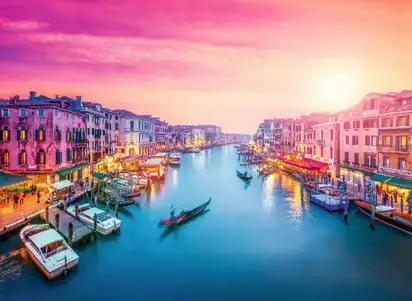 Blick auf den Canal Grande in Venedig bei Sonnenuntergang mit Booten und historischen Gebäuden.