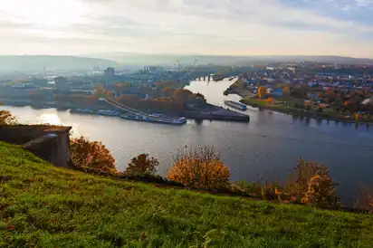 Flusslandschaft mit Stadt im Herbst, Blick von grünen Hügeln auf Wasser und Brücken.