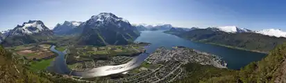 Panorama einer Berglandschaft mit Fluss und Siedlungen am Wasser.