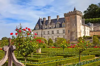 Ein Schloss mit gepflegten Gärten und blühenden Rosen im Vordergrund.