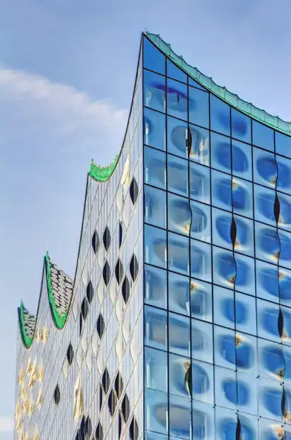 Modernes Gebäude mit wellenförmigem Glasdach vor blauem Himmel.