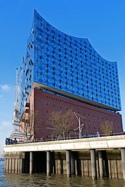 Modernes glasverkleidetes Gebäude mit wellenförmigem Dach am Wasser.
