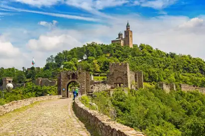 Burg auf einem Hügel mit alten Steinmauern und blauem Himmel im Hintergrund.