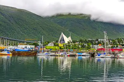 Hafen mit Segelbooten, Bergen im Hintergrund und eine moderne Kathedrale.