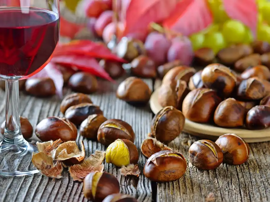 Geröstete Maroni mit Rotwein, weiße und rote Weintrauben im Hintergrund